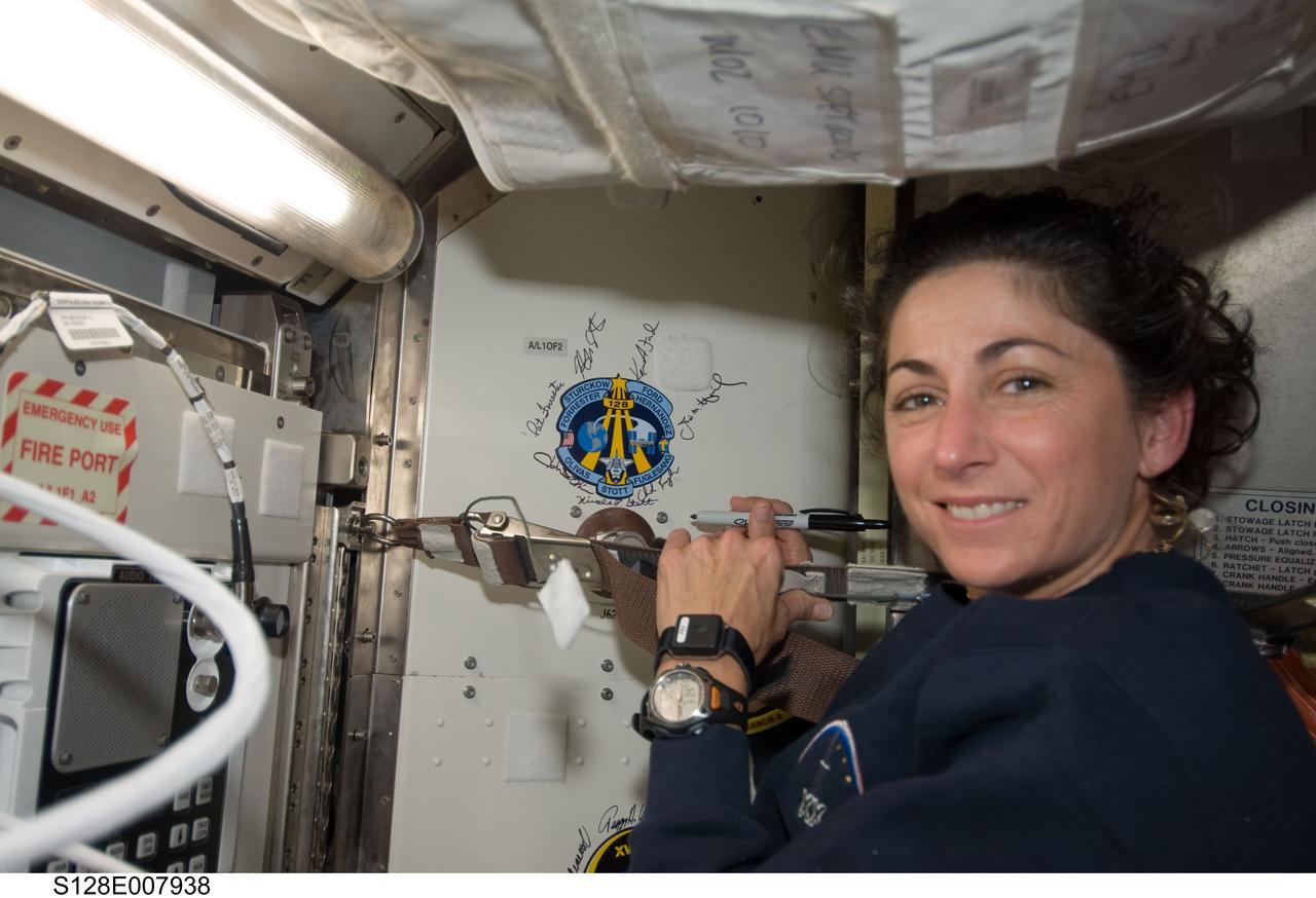 S128-E-007938 (7 Sept. 2009) --- NASA astronaut Nicole Stott, Expedition 20 flight engineer, poses for a photo after signing the STS-128 patch, which was added to the growing collection of insignias representing crews who performed spacewalks from the Quest airlock of the International Space Station.