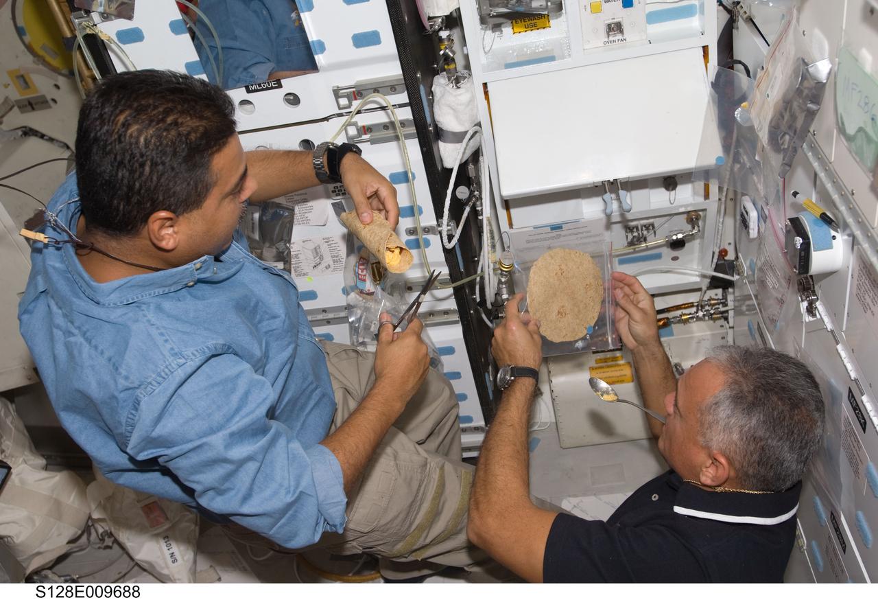 S128-E-009688 (8 Sept. 2009) --- NASA astronauts Jose Hernandez (left) and John “Danny” Olivas, both STS-128 mission specialists, prepare food near the galley on the middeck of Space Shuttle Discovery during flight day 12 activities.