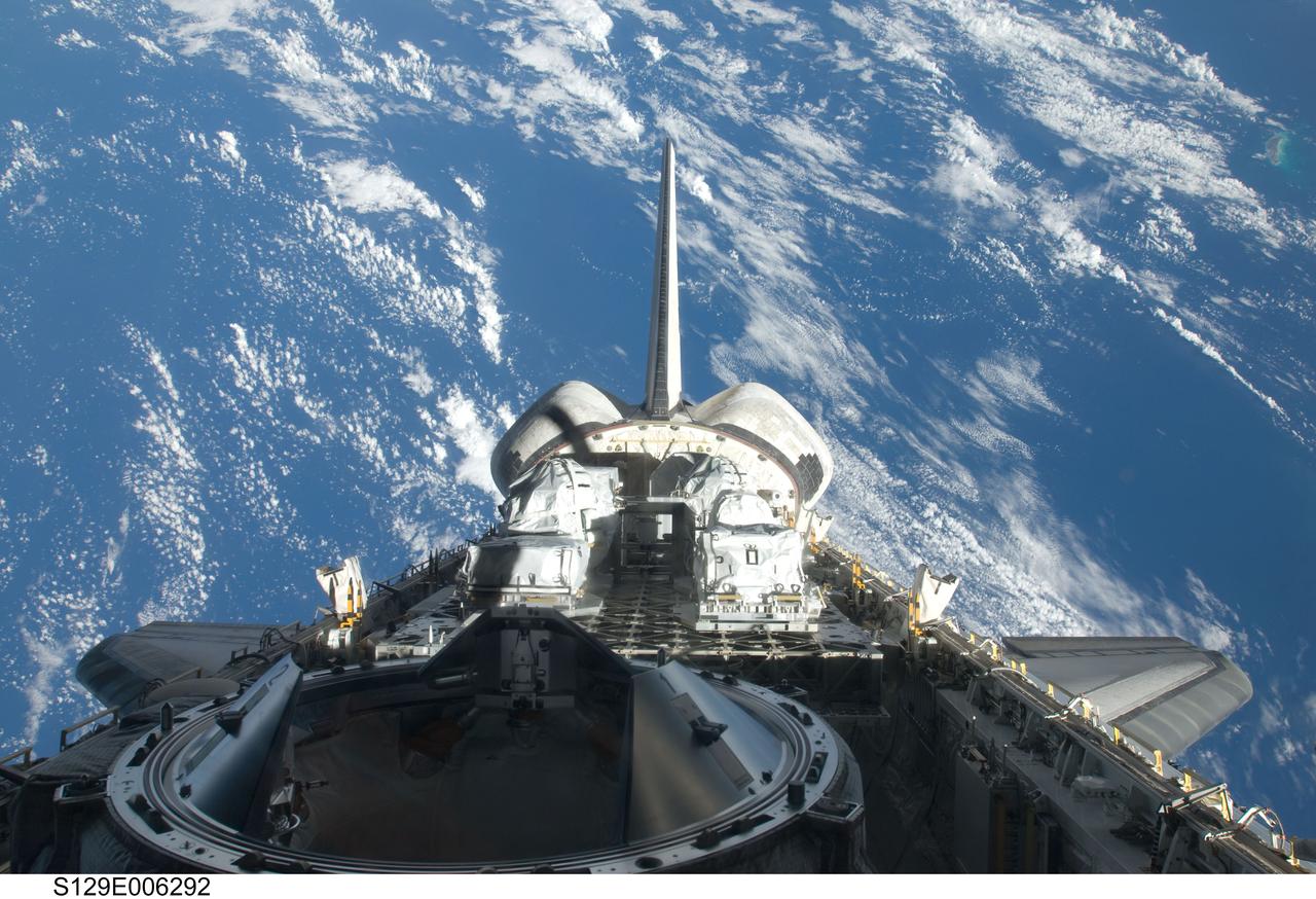 S129-E-006292 (17 Nov. 2009) --- Backdropped by a blue and white part of Earth, a partial view of Space Shuttle Atlantis? payload bay, vertical stabilizer, orbital maneuvering system (OMS) pods and docking mechanism are featured in this image photographed by an STS-129 crew member from an aft flight deck window.