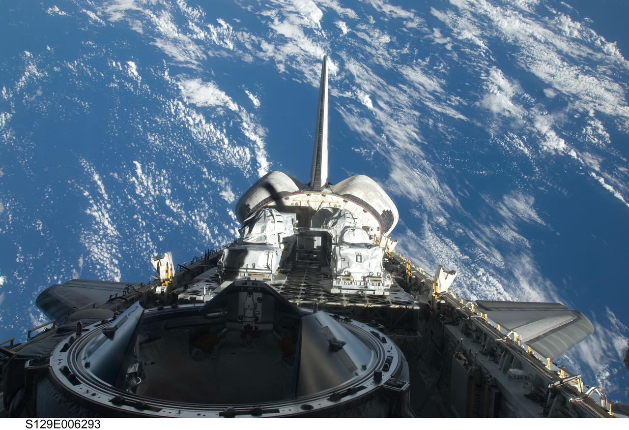 S129-E-006293 (17 Nov. 2009) --- Backdropped by a blue and white part of Earth, a partial view of Space Shuttle Atlantis? payload bay, vertical stabilizer, orbital maneuvering system (OMS) pods and docking mechanism are featured in this image photographed by an STS-129 crew member from an aft flight deck window.