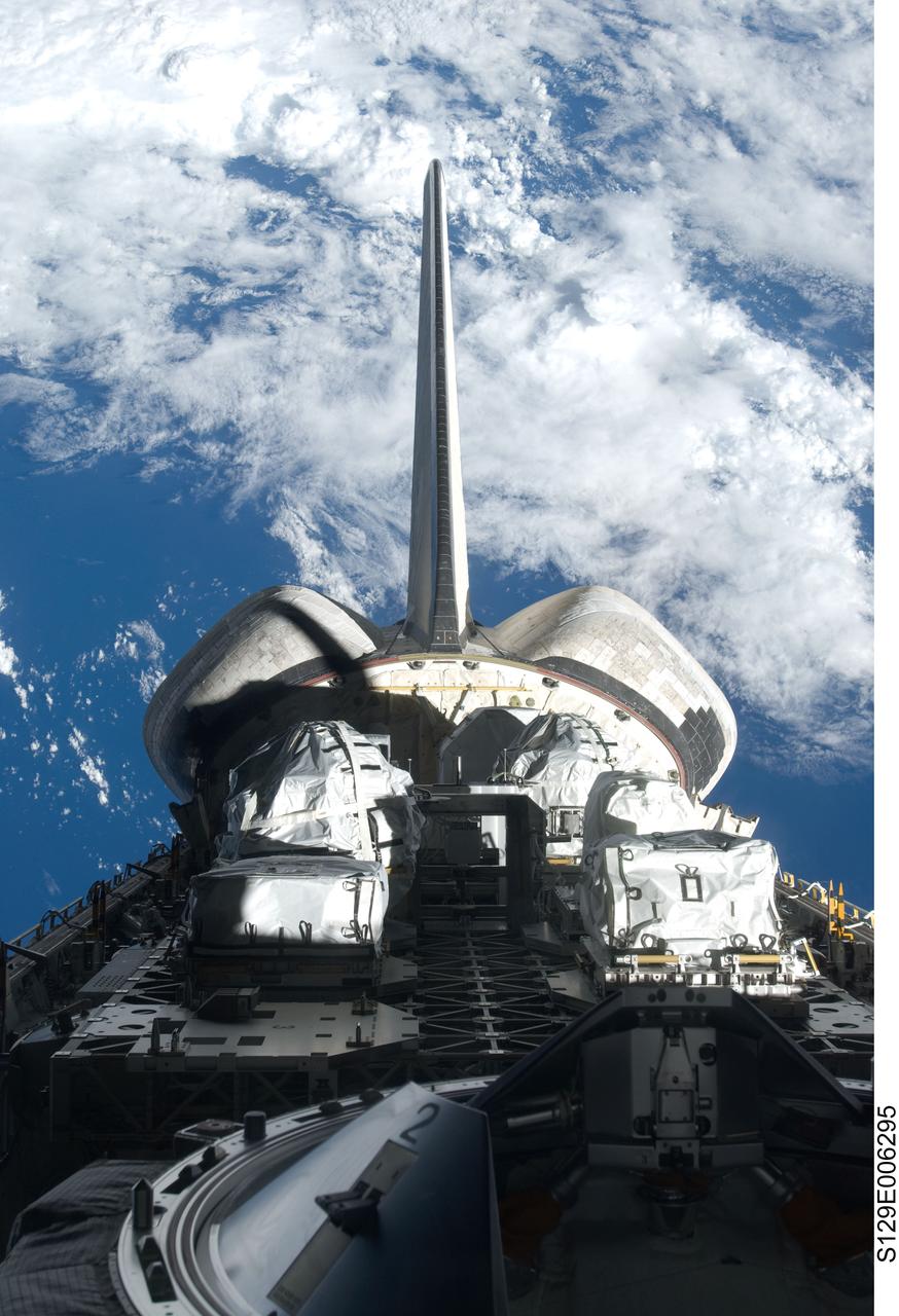 S129-E-006295 (17 Nov. 2009) --- Backdropped by a blue and white part of Earth, a partial view of Space Shuttle Atlantis? payload bay, vertical stabilizer, orbital maneuvering system (OMS) pods and docking mechanism are featured in this image photographed by an STS-129 crew member from an aft flight deck window.