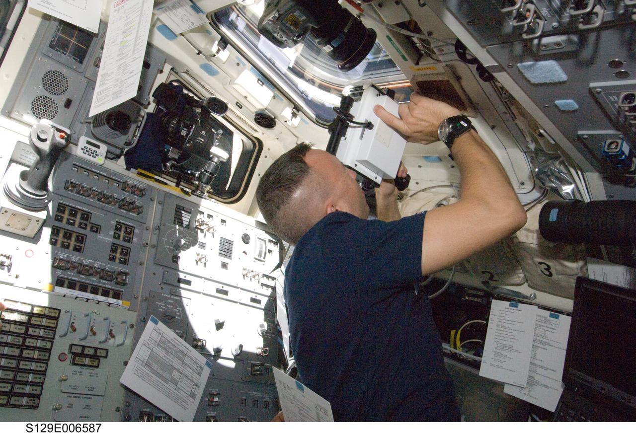 S129-E-006587 (18 Nov. 2009) --- Astronaut Randy Bresnik, STS-129 mission specialist, uses a handheld laser ranging device -- designed to measure the range between two spacecraft -- through one of the overhead windows on the aft flight deck of Space Shuttle Atlantis to track the range of the International Space Station during rendezvous operations.