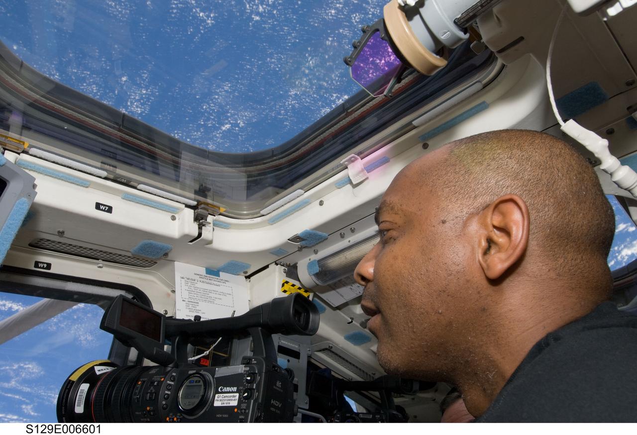 S129-E-006601 (18 Nov. 2009) --- Astronaut Robert L. Satcher Jr., STS-129 mission specialist, uses a High Definition Video (HDV) camera at a window on the aft flight deck of Space Shuttle Atlantis during flight day three activities.