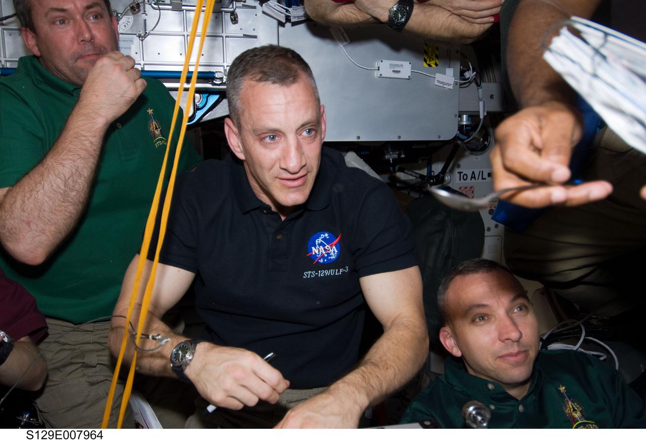 S129-E-007964 (23 Nov. 2009) --- Expedition 21 and STS-129 crew members gather for a meal at the galley in the Unity node of the International Space Station while space shuttle Atlantis remains docked with the station. Pictured are NASA astronauts Charles O. Hobaugh (center), STS-129 commander; along with NASA astronauts Mike Foreman (left) and Randy Bresnik, both STS-129 mission specialists.