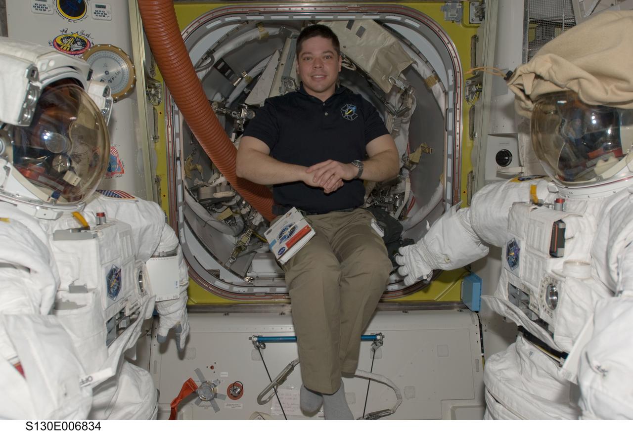 S130-E-006834 (10 Feb. 2010) --- NASA astronaut Robert Behnken, STS-130 mission specialist, poses for a photo between two Extravehicular Mobility Unit (EMU) spacesuits in the Quest airlock of the International Space Station while space shuttle Endeavour remains docked with the station.