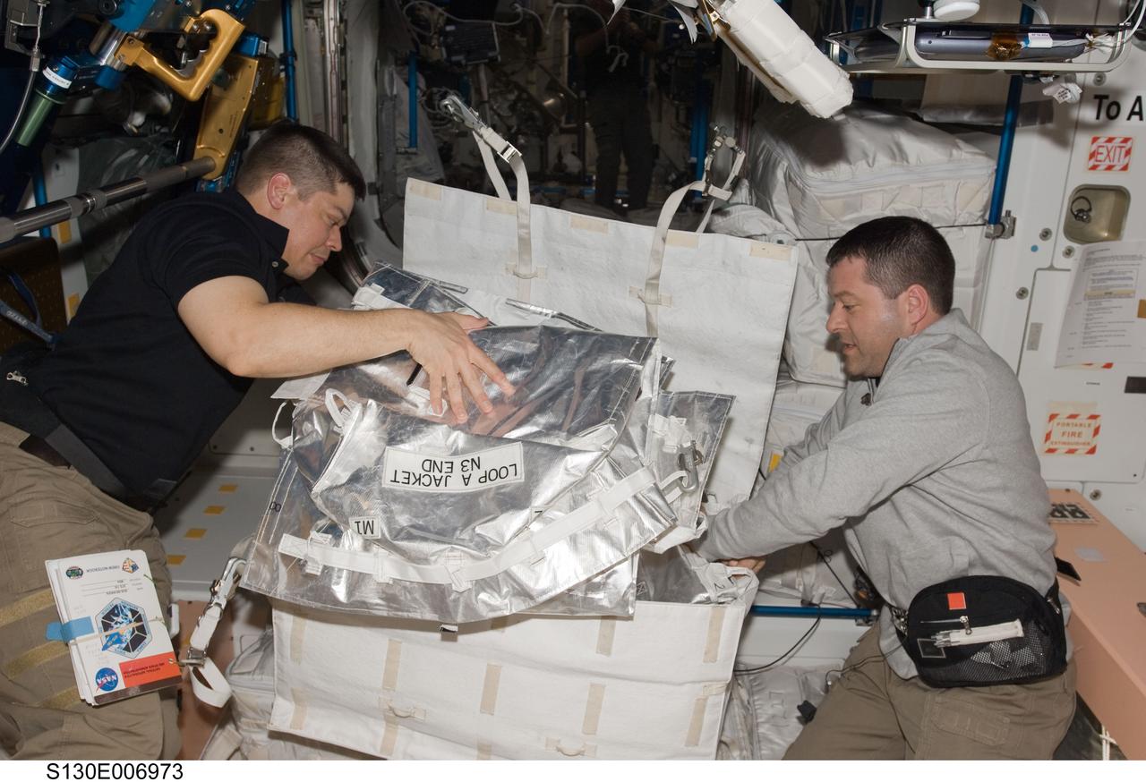 S130-E-006973 (10 Feb. 2010) --- NASA astronauts Robert Behnken (left) and Nicholas Patrick, both STS-130 mission specialists, work with contents of a stowage container in the Unity node of the International Space Station while space shuttle Endeavour remains docked with the station.