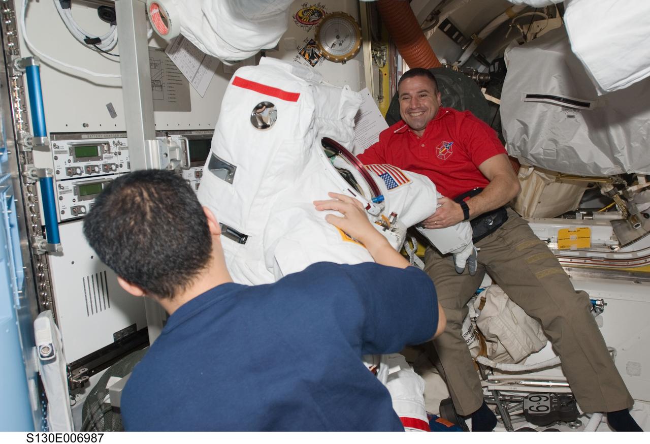 S130-E-006987 (10 Feb. 2010) --- NASA astronaut George Zamka (background), STS-130 commander; and Japan Aerospace Exploration Agency (JAXA) astronaut Soichi Noguchi, Expedition 22 flight engineer, work with an Extravehicular Mobility Unit (EMU) spacesuit in the Quest airlock of the International Space Station while space shuttle Endeavour remains docked with the station.