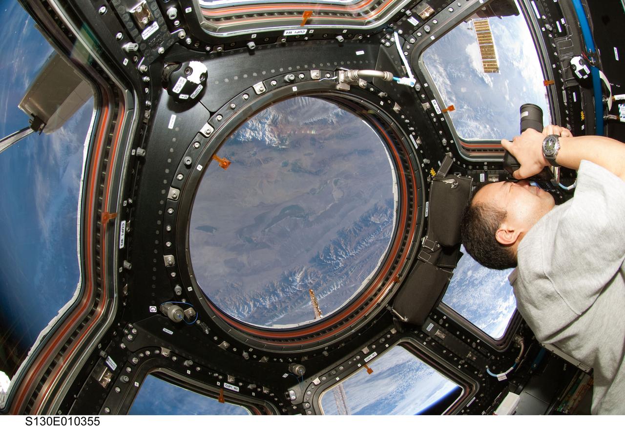 S130-E-010355 (18 Feb. 2010) --- Japan Aerospace Exploration Agency (JAXA) astronaut Soichi Noguchi, Expedition 22 flight engineer, uses a still camera at a window in the Cupola of the International Space Station while space shuttle Endeavour (STS-130) remains docked with the station. The mountains in the center window are the western Burhan Budai Shan (lower right), with Qaidam Basin and lakes, (center), all just north of the city of Golmud, Qinghai Province, China.