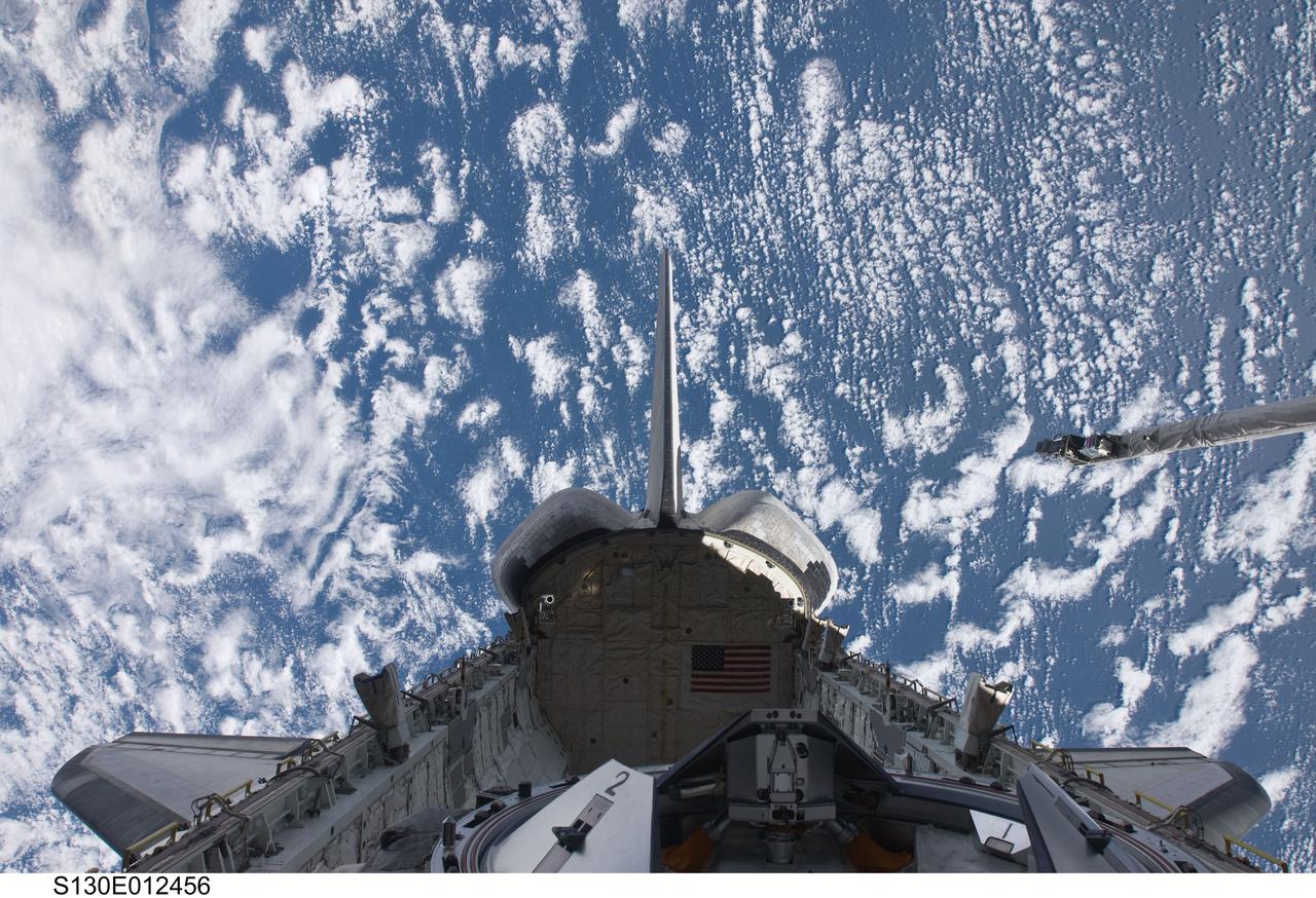 S130-E-012456 (20 Feb. 2010) --- Backdropped by a blue and white part of Earth, a partial view of space shuttle Endeavour's payload bay, vertical stabilizer, orbital maneuvering system (OMS) pods and docking mechanism are featured in this image photographed by an STS-130 crew member from an aft flight deck window.