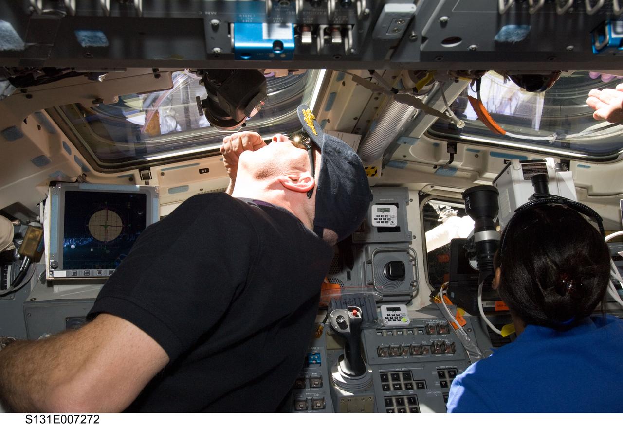 S131-E-007272 (7 April 2010) --- NASA astronauts Alan Poindexter, STS-131 commander; and Stephanie Wilson, mission specialist, look through overhead windows on the aft flight deck of space shuttle Discovery during flight day three activities. Wilson is using a handheld laser ranging device -- designed to measure the range between two spacecraft.