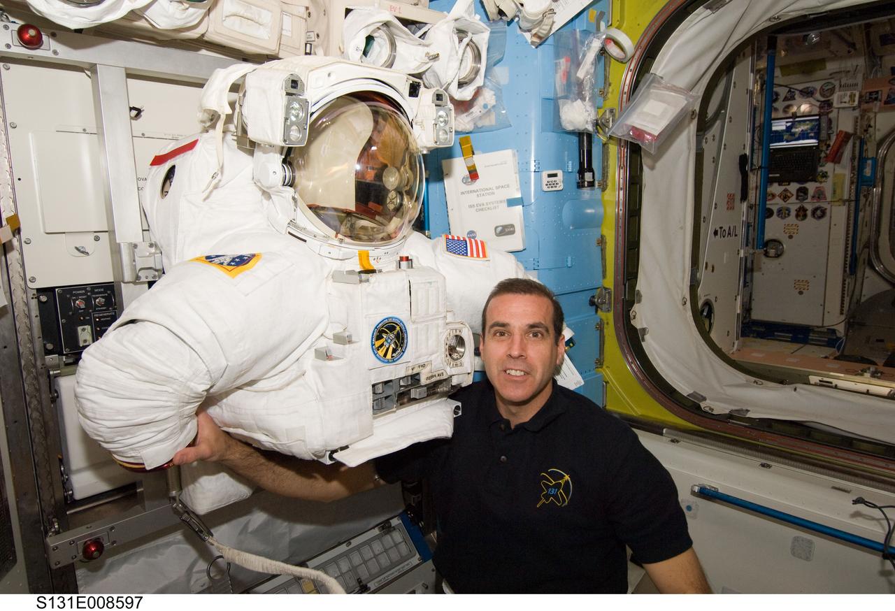 S131-E-008597 (10 April 2010) --- NASA astronaut Rick Mastracchio, STS-131 mission specialist, poses for a photo with the torso portion of his Extravehicular Mobility Unit (EMU) spacesuit in the Quest airlock of the International Space Station while space shuttle Discovery remains docked with the station.
