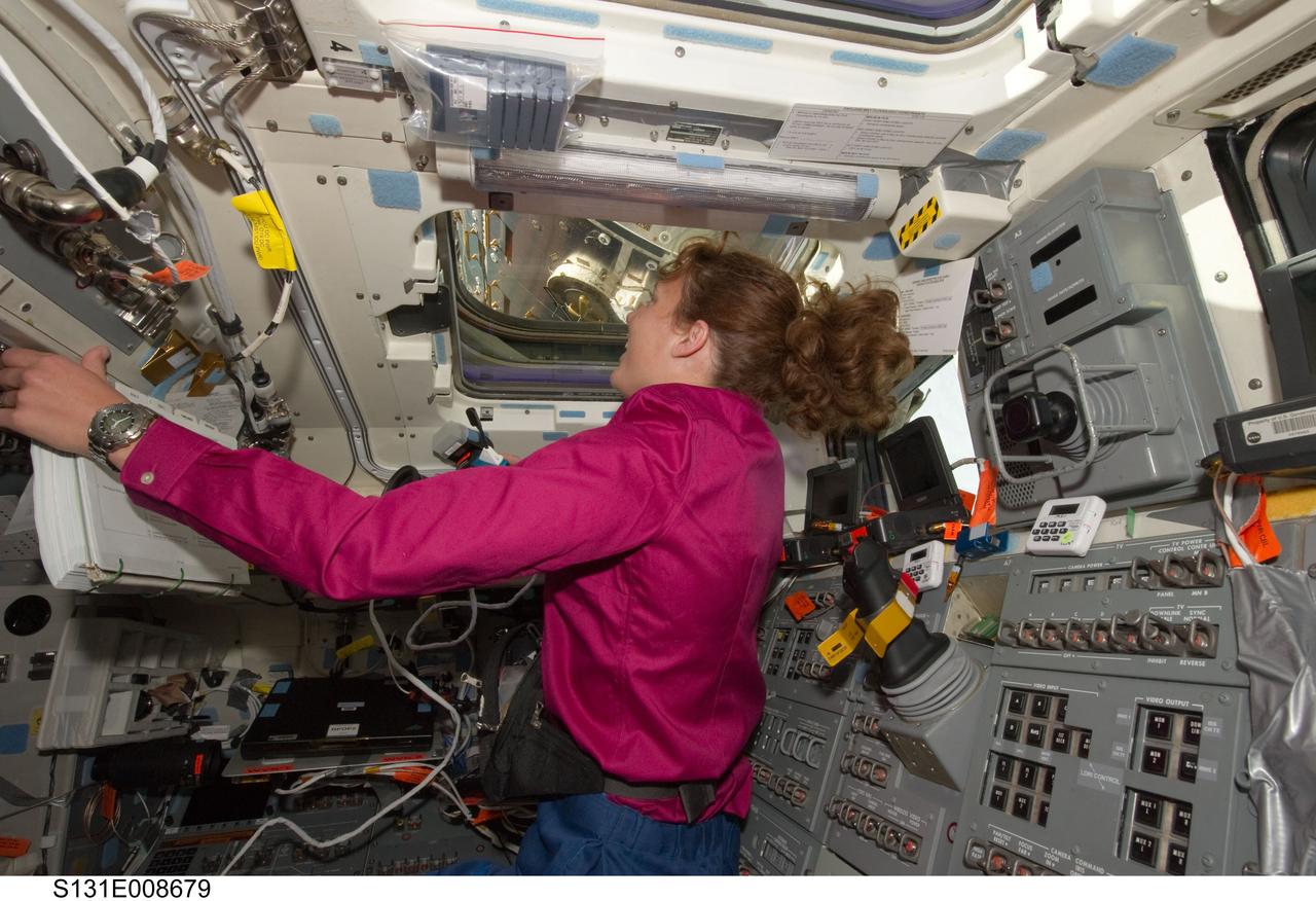 S131-E-008679 (11 April 2010) --- NASA astronaut Dorothy Metcalf-Lindenburger, STS-131 mission specialist, looks through an overhead window on the aft flight deck of space shuttle Discovery while docked with the International Space Station.