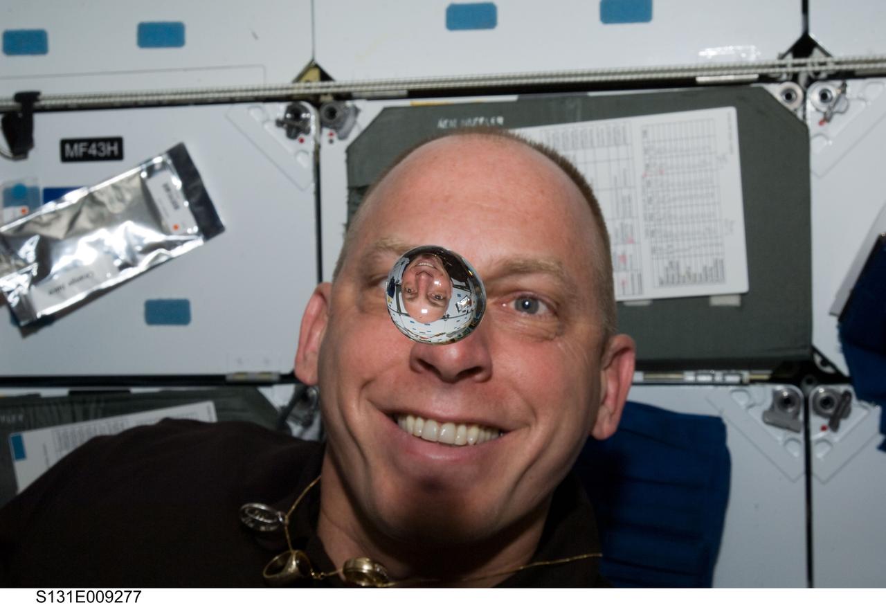 S131-E-009277 (12 April 2010) --- NASA astronaut Clayton Anderson, STS-131 mission specialist, watches a water bubble float freely between him and the camera, showing his image refracted, on the middeck of space shuttle Discovery while docked with the International Space Station.
