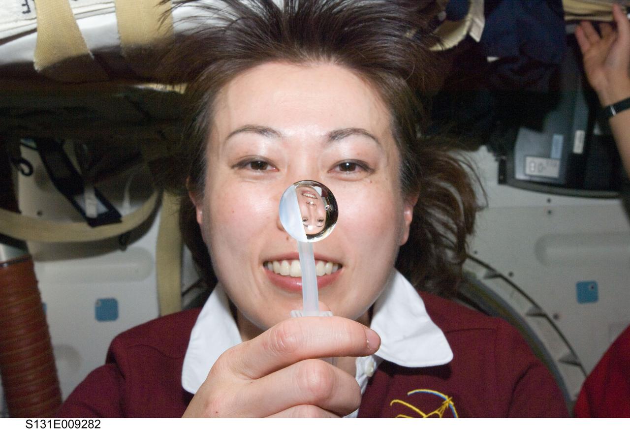 S131-E-009282 (12 April 2010) --- Japan Aerospace Exploration Agency (JAXA) astronaut Naoko Yamazaki, STS-131 mission specialist, squeezes a water bubble out of her beverage container, showing her image refracted, on the middeck of space shuttle Discovery while docked with the International Space Station.