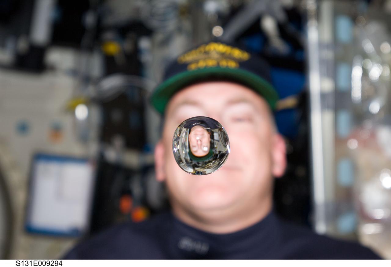 S131-E-009294 (12 April 2010) --- NASA astronaut Alan Poindexter, STS-131 commander, watches a water bubble float freely between him and the camera, showing his image refracted, on the middeck of space shuttle Discovery while docked with the International Space Station.
