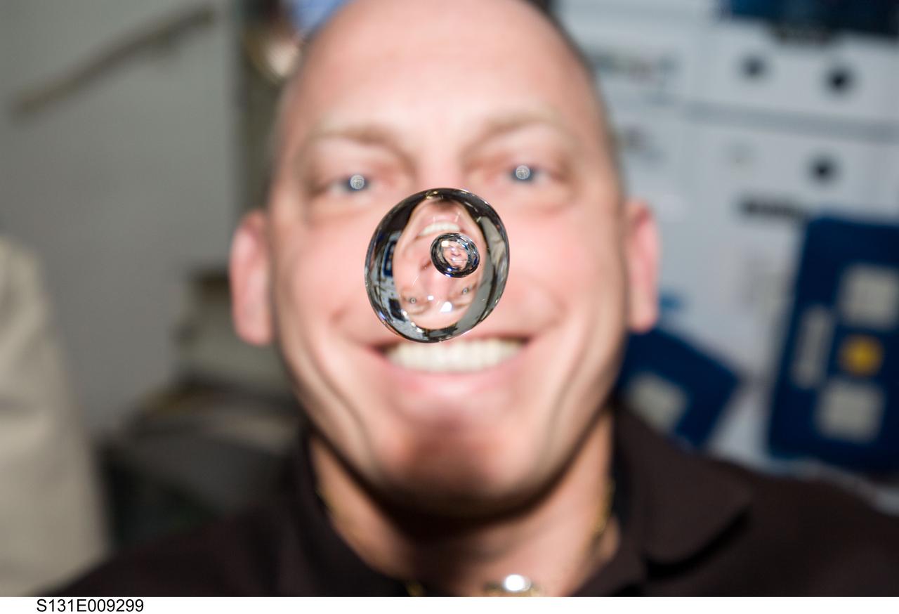 S131-E-009299 (12 April 2010) --- NASA astronaut Clayton Anderson, STS-131 mission specialist, watches a water bubble float freely between him and the camera, showing his image refracted, on the middeck of space shuttle Discovery while docked with the International Space Station.