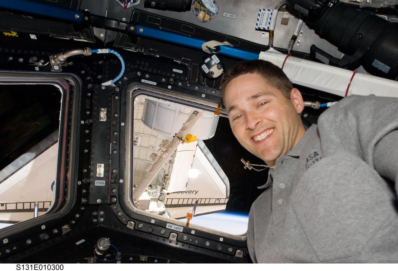 S131-E-010300 (15 April 2010) --- NASA astronaut James P. Dutton Jr., STS-131 pilot, poses for a photo near the windows in the Cupola of the International Space Station while space shuttle Discovery (visible through the windows) remains docked with the station.