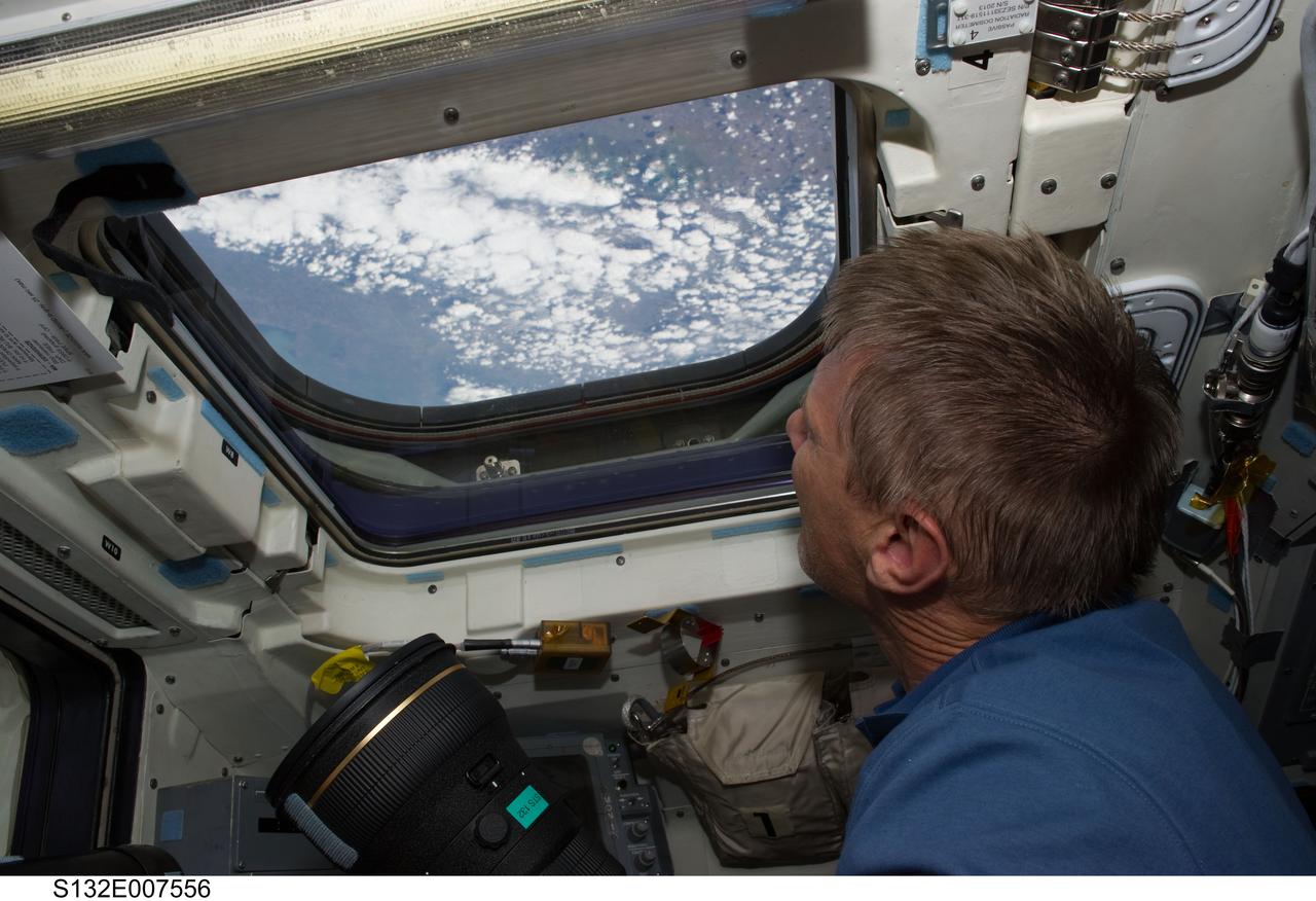 S132-E-007556 (15 May 2010) --- NASA astronaut Piers Sellers, STS-132 mission specialist, holds a still camera while looking through an overhead window on the aft flight deck of the Earth-orbiting space shuttle Atlantis during flight day two activities.