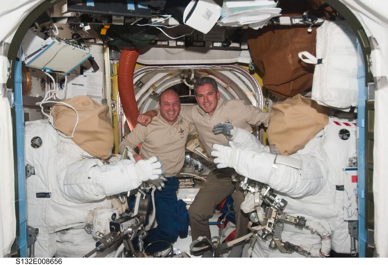 S132-E-008656 (20 May 2010) --- NASA astronauts Garrett Reisman (left) and Michael Good, both STS-132 mission specialists, pose for a photo between two Extravehicular Mobility Unit (EMU) spacesuits in the Quest airlock of the International Space Station while space shuttle Atlantis remains docked with the station.