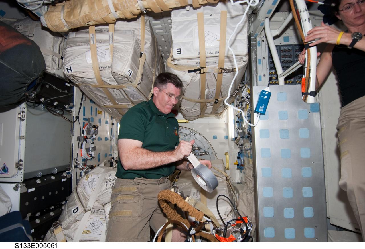 S133-E-005061 (25 Feb. 2011) --- Astronauts Steve Bowen and Nicole Stott, both STS-133 mission specialists, are seen at work on the middeck of the space shuttle Discovery on flight day two. Photo credit: NASA or National Aeronautics and Space Administration