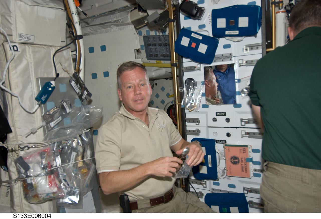 S133-E-006004 (25 Feb. 2011) --- Astronauts Steve Lindsey (left), STS-133 commander, and Steve Bowen, mission specialist, take a break from flight day 2 duties on Discovery's middeck. Lindsey is preparing a snack, as the shuttle makes its way toward a weekend docking with the International Space Station. Photo credit: NASA or National Aeronautics and Space Administration