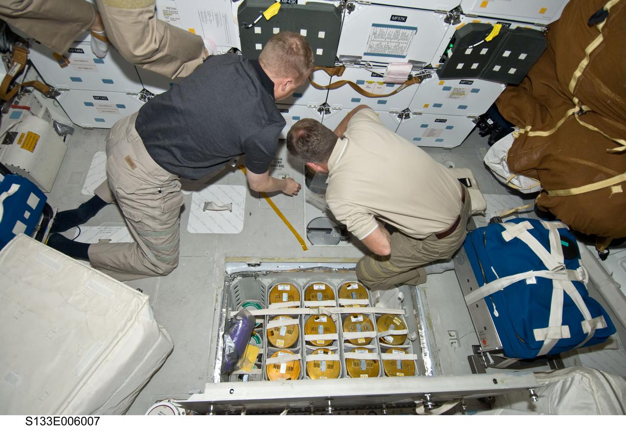 S133-E-006007 (25 Feb. 2011) --- On space shuttle Discovery’s middeck, astronauts Steve Lindsey (right), STS-133 commander, and Eric Boe, pilot, work with lithium hydroxide canisters beneath the floor, performing the same house-keeping chore accomplished by many astronauts in the 30-year history of the Space Shuttle Program. Photo credit: NASA or National Aeronautics and Space Administration
