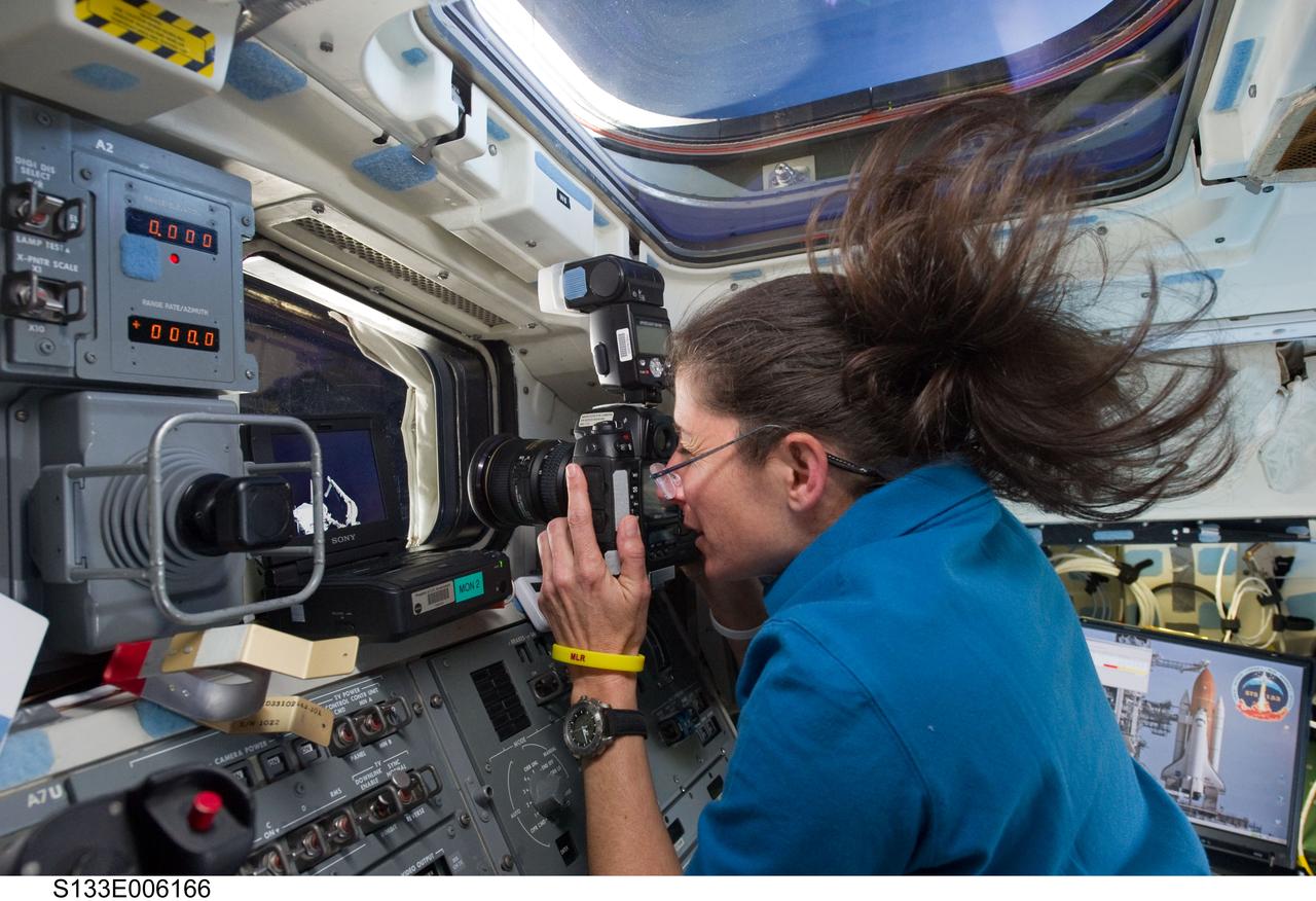 S133-E-006166 (25 Feb. 2011) --- NASA astronaut Nicole Stott, STS-133 mission specialist, uses a still camera at a window on the aft flight deck of space shuttle Discovery during flight day two activities. Photo credit: NASA or National Aeronautics and Space Administration