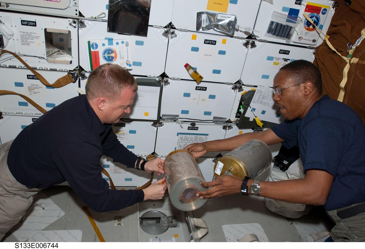 S133-E-006744 (26 Feb. 2011) --- On space shuttle Discovery's middeck, astronauts Eric Boe (left), STS-133 pilot; and Alvin Drew, mission specialist, work with lithium hydroxide canisters beneath the floor, performing the same house-keeping chore accomplished by many astronauts in the 30-year history of the Space Shuttle Program. Photo credit: NASA or National Aeronautics and Space Administration