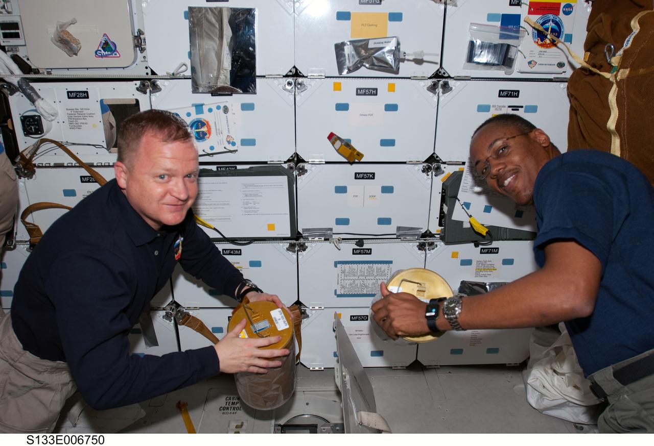 S133-E-006750 (26 Feb. 2011) --- On space shuttle Discovery's middeck, astronauts Eric Boe (left), STS-133 pilot; and Alvin Drew, mission specialist, work with lithium hydroxide canisters beneath the floor, performing the same house-keeping chore accomplished by many astronauts in the 30-year history of the Space Shuttle Program. Photo credit: NASA or National Aeronautics and Space Administration