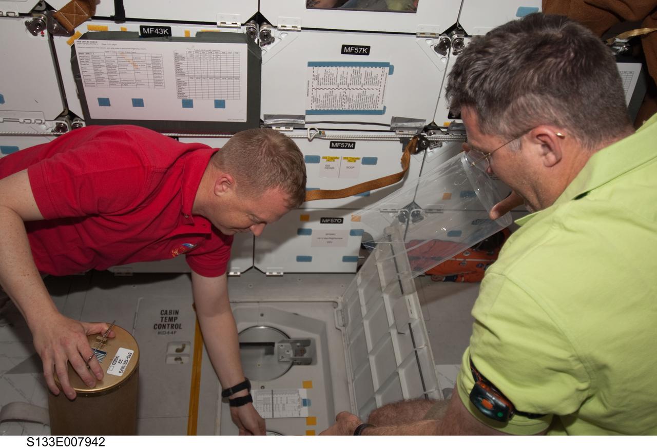 S133-E-007942 (28 Feb. 2011) --- NASA astronauts Eric Boe (left), STS-133 pilot; and Steve Bowen, mission specialist, work with lithium hydroxide (LiOH) canisters from beneath space shuttle Discovery’s middeck while docked with the International Space Station. Photo credit: NASA or National Aeronautics and Space Administration