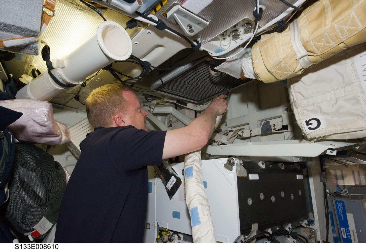 S133-E-008610 (3 March 2011) --- NASA astronaut Eric Boe, STS-133 pilot, uses a vacuum cleaner to remove dust particles from the air filter system on the middeck of space shuttle Discovery while docked with the International Space Station. Photo credit: NASA or National Aeronautics and Space Administration