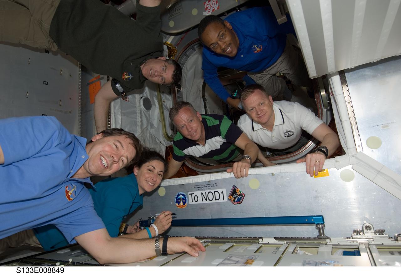 S133-E-008849 (5 March 2011) --- In the newly-installed Permanent Multipurpose Module (PMM), the STS-133 crew members pose while signing the STS-133 patch, which was added to the growing collection of insignias representing crews who have worked on the International Space Station. Pictured counter-clockwise (from the center) are NASA astronauts Steve Lindsey, commander; Eric Boe, pilot; Alvin Drew, Steve Bowen, Nicole Stott and Michael Barratt, all mission specialists. Photo credit: NASA or National Aeronautics and Space Administration