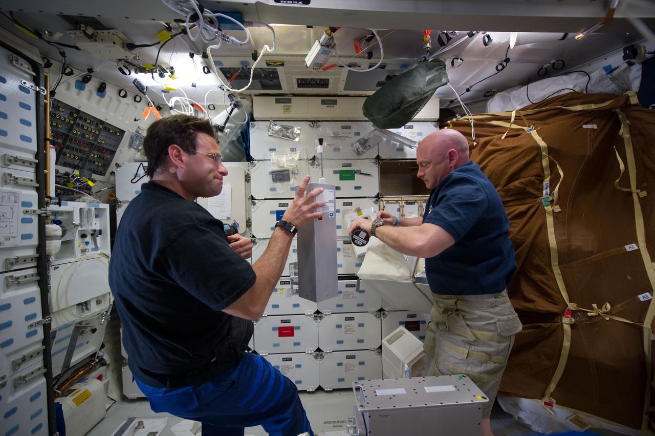 S134-E-006436 (17 May 20110) --- NASA astronauts Greg Chamitoff (left), mission specialist, and Mark Kelly, mission commander, work on separate chores on Endeavour's middeck during the second flight day of the STS-134 mission. Chamitoff is holding Cube Lab Module ? 8. Kelly is unpacking canisters of the Group Activation Pack. Endeavour and its crew of six astronauts will arrive at the International Space Station in less than 24 hours. Photo credit: NASA