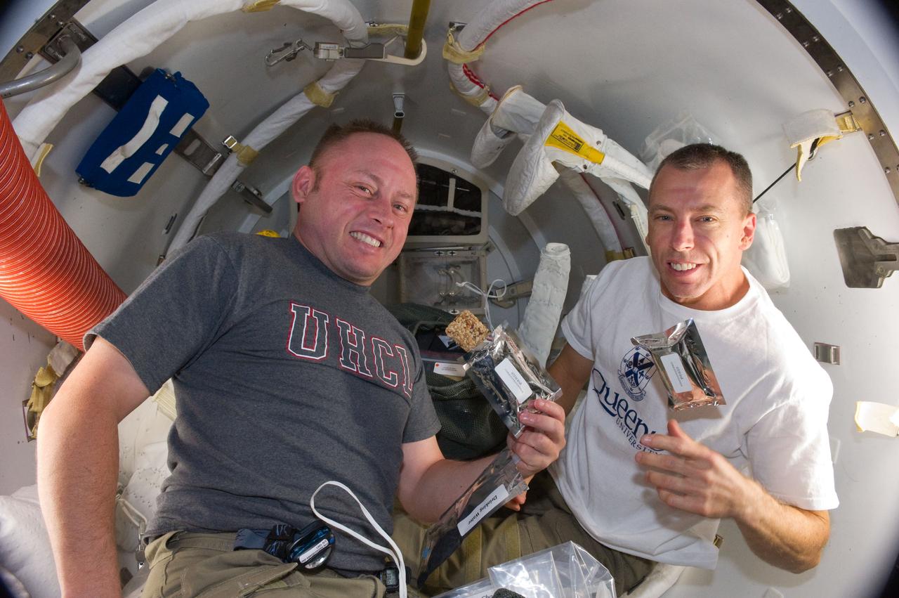 S134-E-008462 (22 May 2011) --- A short time before they donned their Extravehicular Mobility Unit spacesuits, NASA astronauts Michael Fincke (left) and Andrew Feustel, both STS-134 mission specialists, ate breakfast snacks onboard the International Space Station (ISS). Once outside the orbiting complex,   Fincke and Feustel coordinated their shared activity with NASA astronaut Greg Chamitoff (out of frame), who stayed in communication with the pair and with Mission Control Center in Houston from the shirt sleeve environment inside the ISS.  Photo credit: NASA