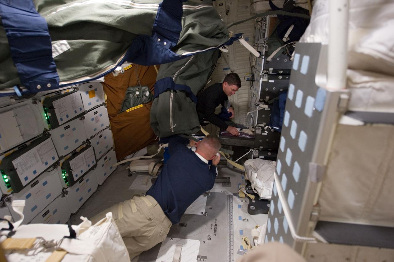 S135-E-006255 (8 July 2011) --- NASA astronauts Rex Walheim (top of frame), mission specialist, and Doug Hurley, pilot, are surrounded by supplies and equipment on the middeck of the space shuttle Atlantis on route to the International Space Station. Photo credit: NASA