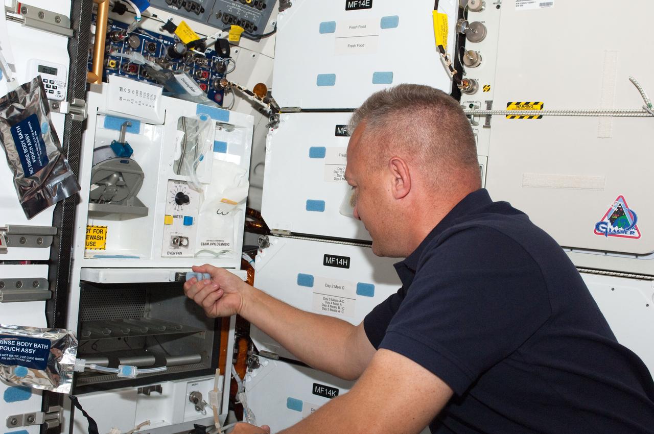 S135-E-007698 (13 July 2011) --- Taking a brief break from moving chores and other busy activities on the joint shuttle/International Space Station complex, NASA astronaut Doug Hurley prepares a meal at Atlantis' middeck galley. July 13 marks the sixth day in space for the STS-135 pilot and his three crewmates. Photo credit: NASA
