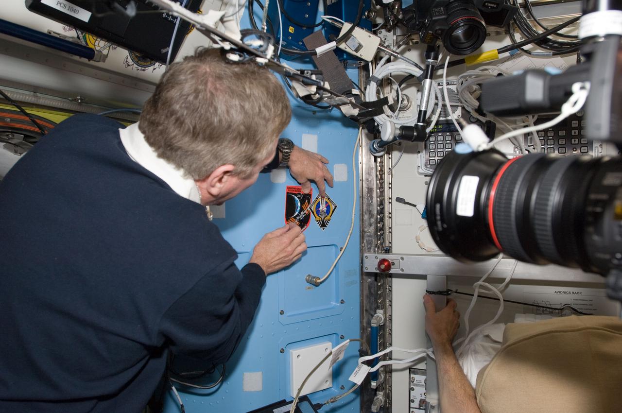 S135-E-009484 (18 July 2011) --- In the Quest airlock of the International Space Station, NASA astronaut Mike Fossum, Expedition 28 flight engineer, draws attention to the freshly posted STS-135 decal next to that of him and his five crewmates. Photo credit: NASA