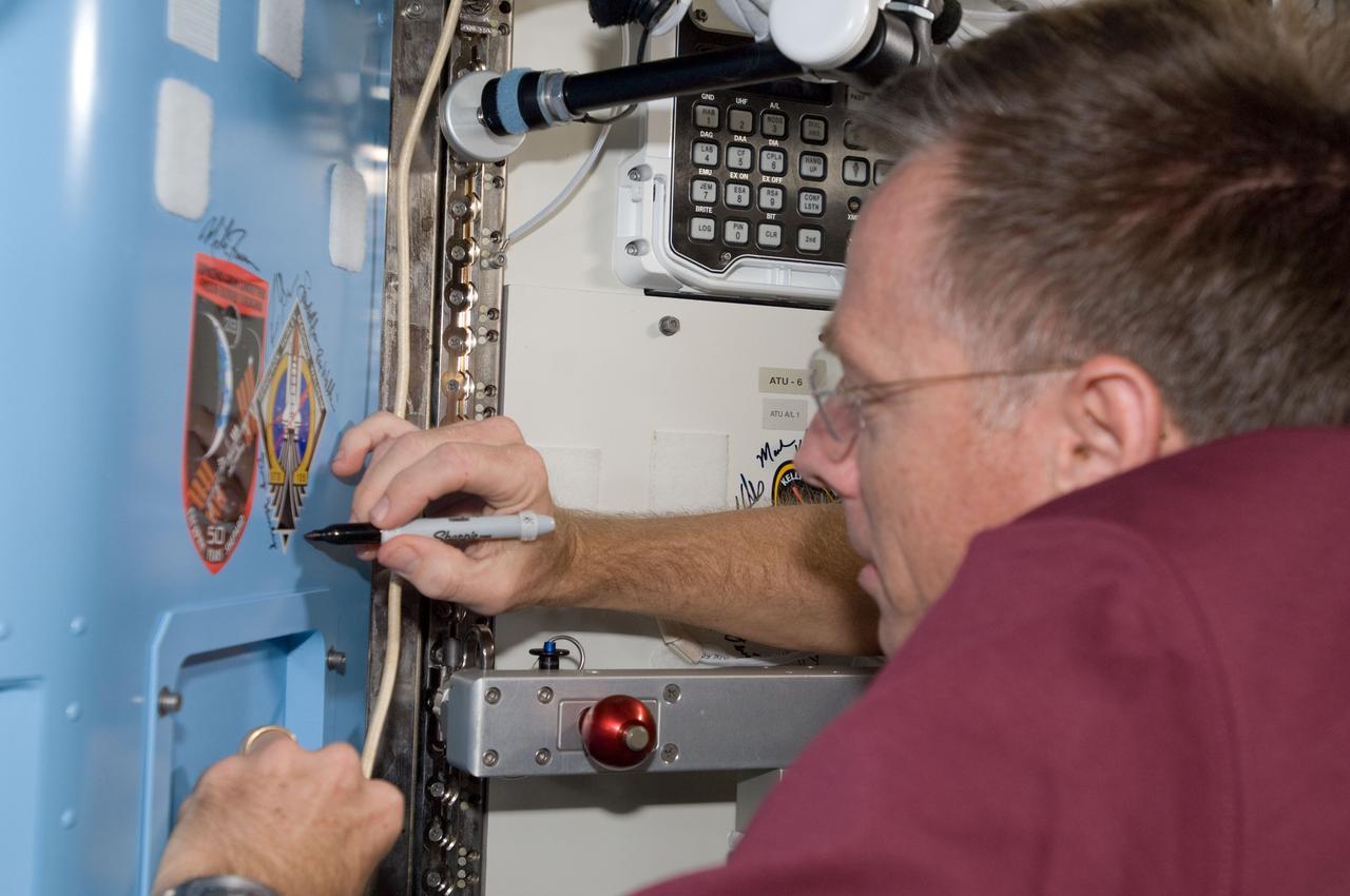 S135-E-009493 (18 July 2011) --- NASA astronaut Chris Ferguson, STS-135 commander, signs an insignia decal for his mission in the Quest airlock of the International Space Station. The shuttle insignia is mounted next to that of the Expedition 28. Having docked Atlantis to the station over a week ago, Ferguson and three crewmates are preparing to undock from the station early on July 19 and prepare for a July 21 landing in Florida. Photo credit: NASA