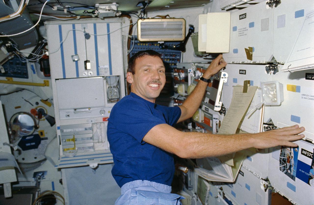STS026-06-033 (5 Oct 1988)  --- Astronaut David C. Hilmers, STS-26 mission specialist,  reads teleprinted message which has been clipped to stowage locker doors on  the middeck.  Food, a galley and various experiments surround the mission specialist.