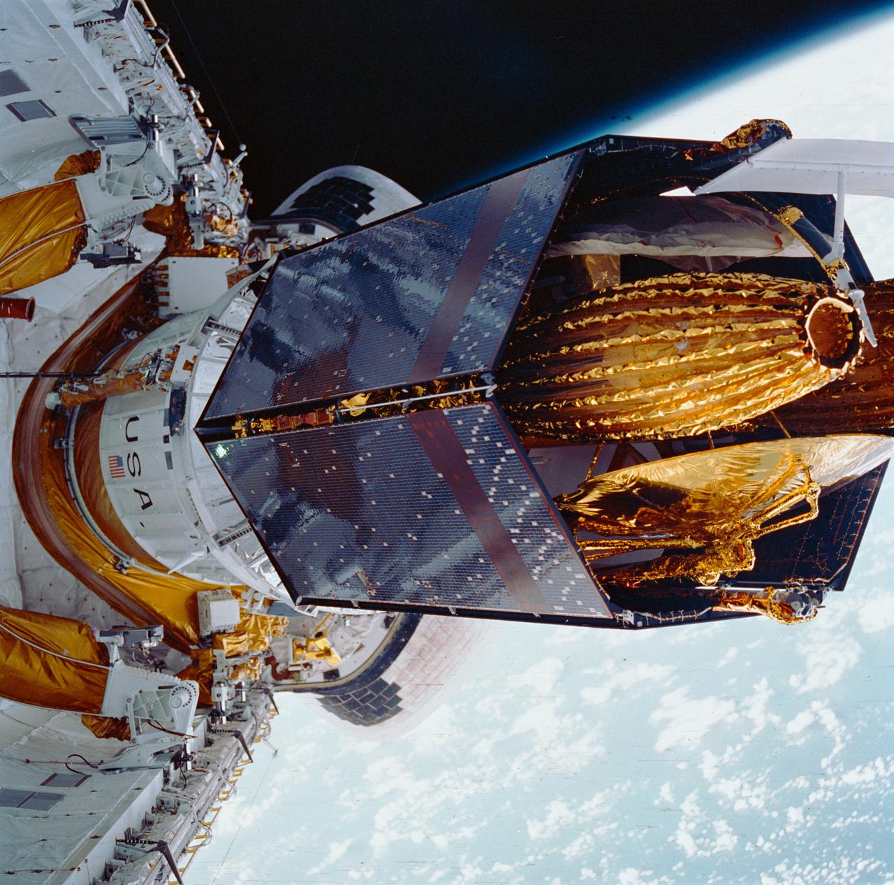 During STS-26, inertial upper stage (IUS) with tracking and data relay satellite C (TDRS-C) located in the payload bay (PLB) of Discovery, Orbiter Vehicle (OV) 103, is positioned into its proper deployment attitude (an angle of 50 degrees) by the airborne support equipment (ASE). In the foreground, the ASE forward cradle is visible. The IUS is mounted in the ASE aft frame tilt actuator (AFTA) table. TDRS-C components in stowed configuration include solar array panels, TDRS single access #1 and #2, TDRS SGL, and S-Band omni antenna. In the background are the orbital maneuvering system (OMS) pods, the Earth's cloud-covered surface, and the Earth's limb.