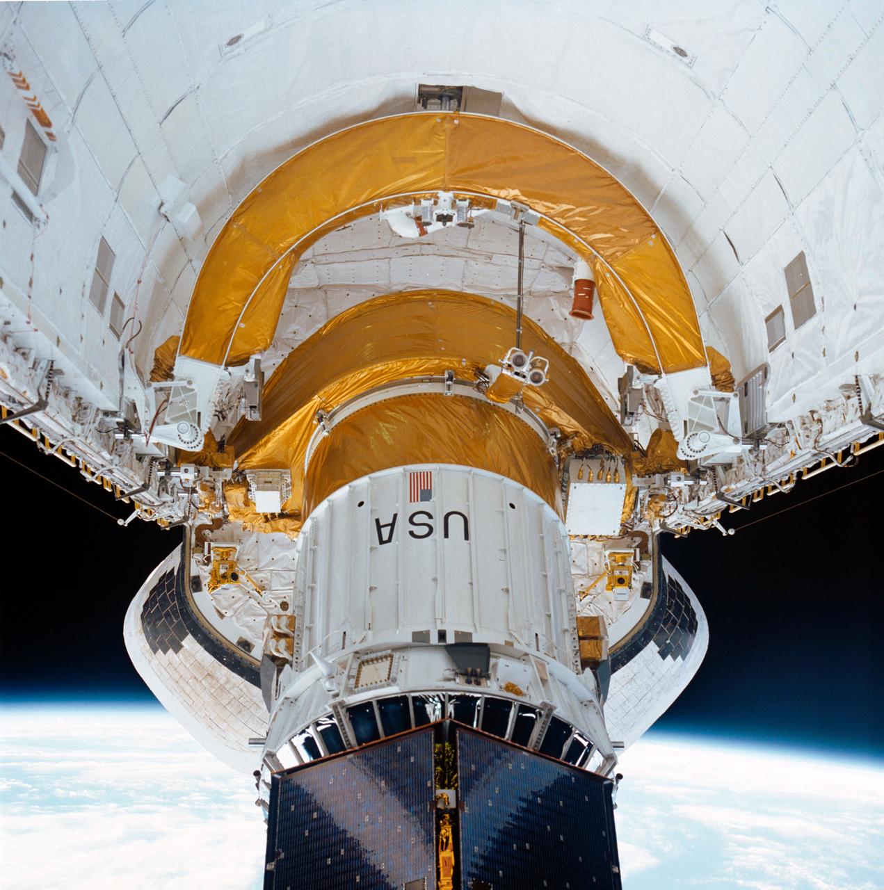 During STS-26, inertial upper stage (IUS) with the tracking and data relay satellite C (TDRS-C) located in the payload bay (PLB) of Discovery, Orbiter Vehicle (OV) 103, is raised into deployment attitude (an angle of 50 degrees) by the airborne support equipment (ASE). ASE aft frame tilt actuator (AFTA) table supports the IUS as it is positioned in the PLB and the ASE umbilical boom drifts away from IUS toward ASE forward cradle. TDRS-C solar array panels (in stowed configuration) are visible on top of the IUS. In the background are the orbital maneuvering system (OMS) pods and the Earth's limb.