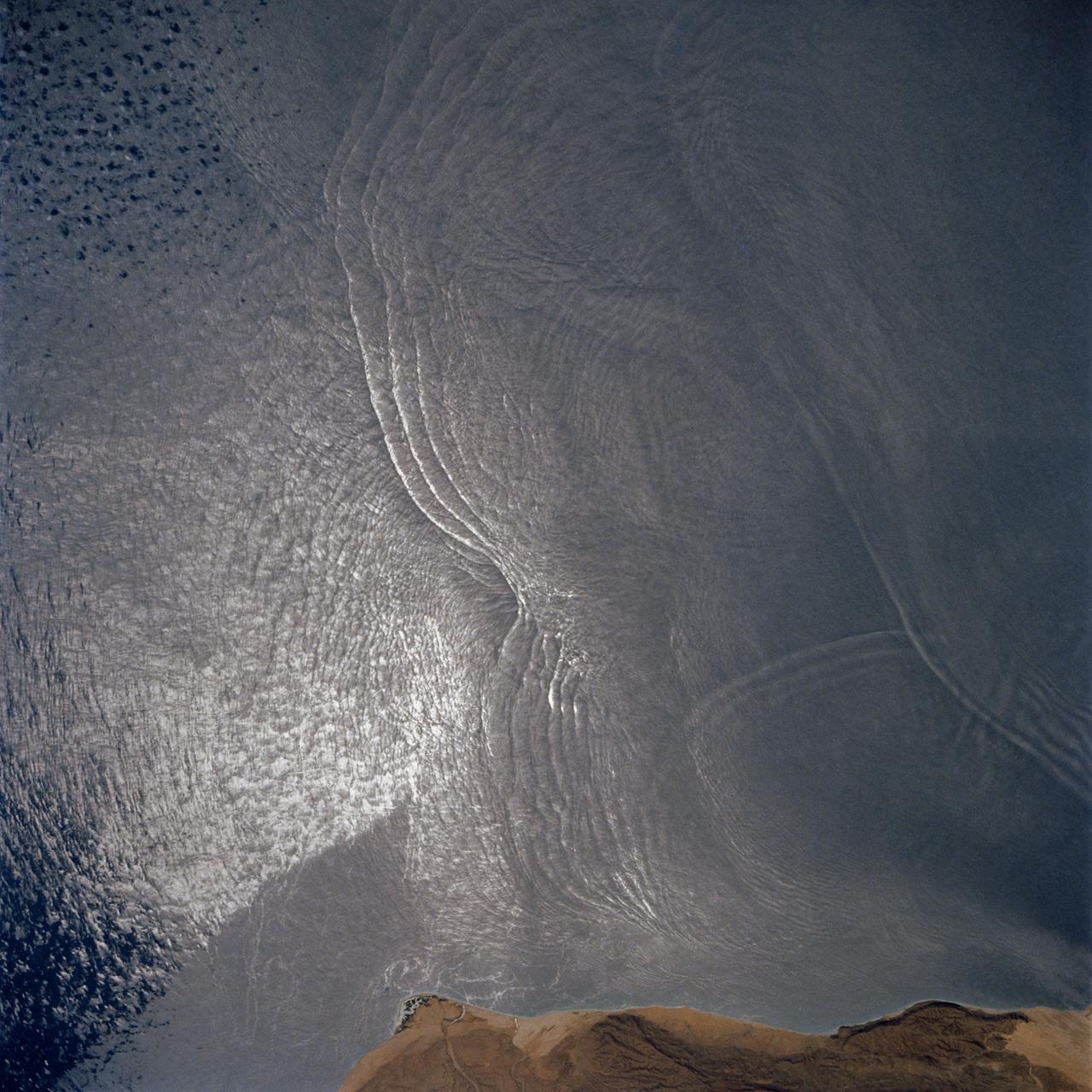 The arculate fronts of these apparently converging internal waves off the northeast coast of Somalia (11.5N, 51.5E) probably were produced by interaction with two parallel submarine canyons off the Horn of Africa. Internal waves are packets of tidally generated waves traveling within the ocean at varying depths and are not detectable by any surface disturbance.
