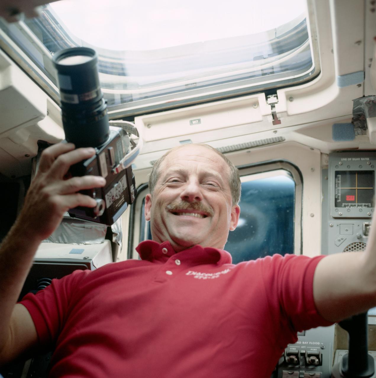 STS026-47-013 (5 Oct 1988) --- Astronaut Frederick H. (Rick) Hauck, commander, on the flight deck, with one of the many cameras carried onboard Discovery to renew documentation of planet Earth.  This particular camera is a 70mm handheld Hasselblad.
