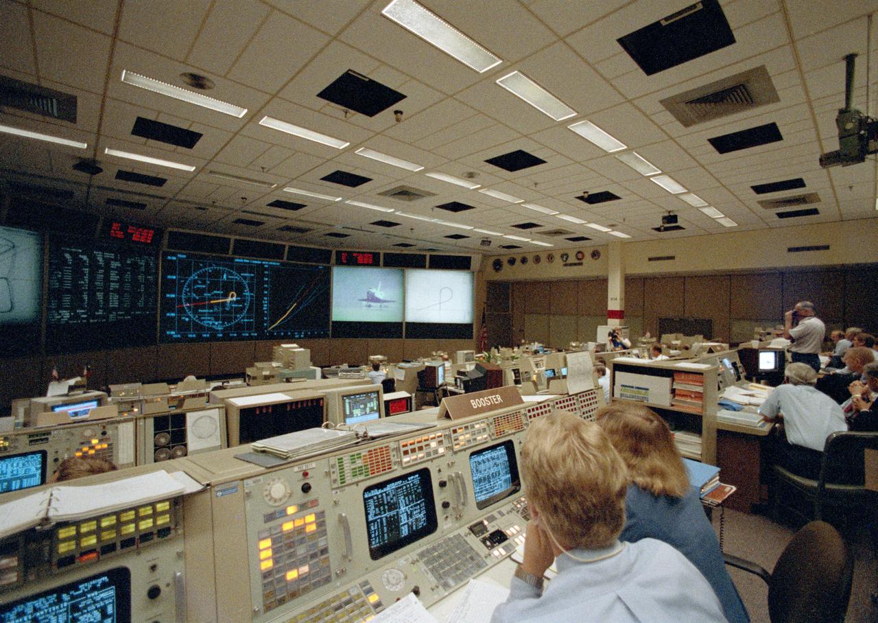 STS026-S-117 (3 Oct 1988) --- Flight controllers in Houston witness the landing of the Space Shuttle Discovery on a dry lake bed at NASA?s Dryden Flight Research Facility. The orbiter is seen on the giant screen in front of the flight control room just as the landing gear touches down.