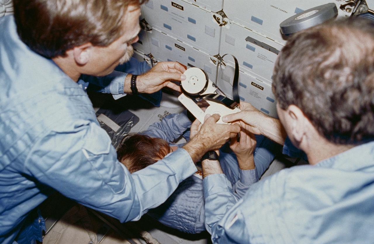 STS027-05-020 (2-6 Dec. 1988) --- In the foreground, astronauts Robert L. Gibson (left) and Guy S. Gardner, commander and pilot, respectively, for the STS-27 mission, repair a 3/4-inch video reel on the middeck of the Earth-orbiting space shuttle Atlantis. Photo credit: NASA
