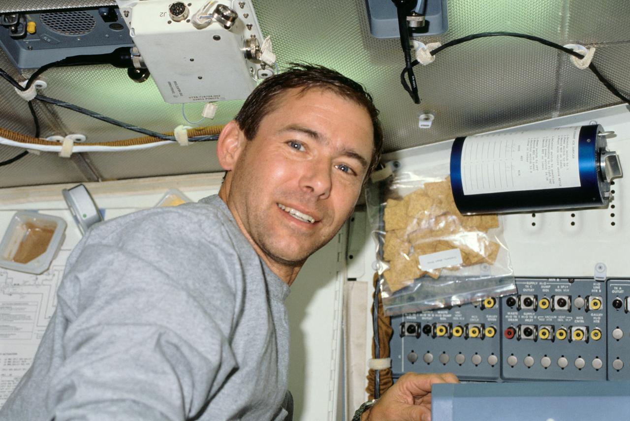 STS028-11-017 (August 1989) --- Astronaut Brewster H. Shaw Jr., mission commander, is captured with a 35mm camera on the middeck of the space shuttle Columbia during the STS-28 flight. Nearby are a couple of beverage containers and a packet of wheat crackers.