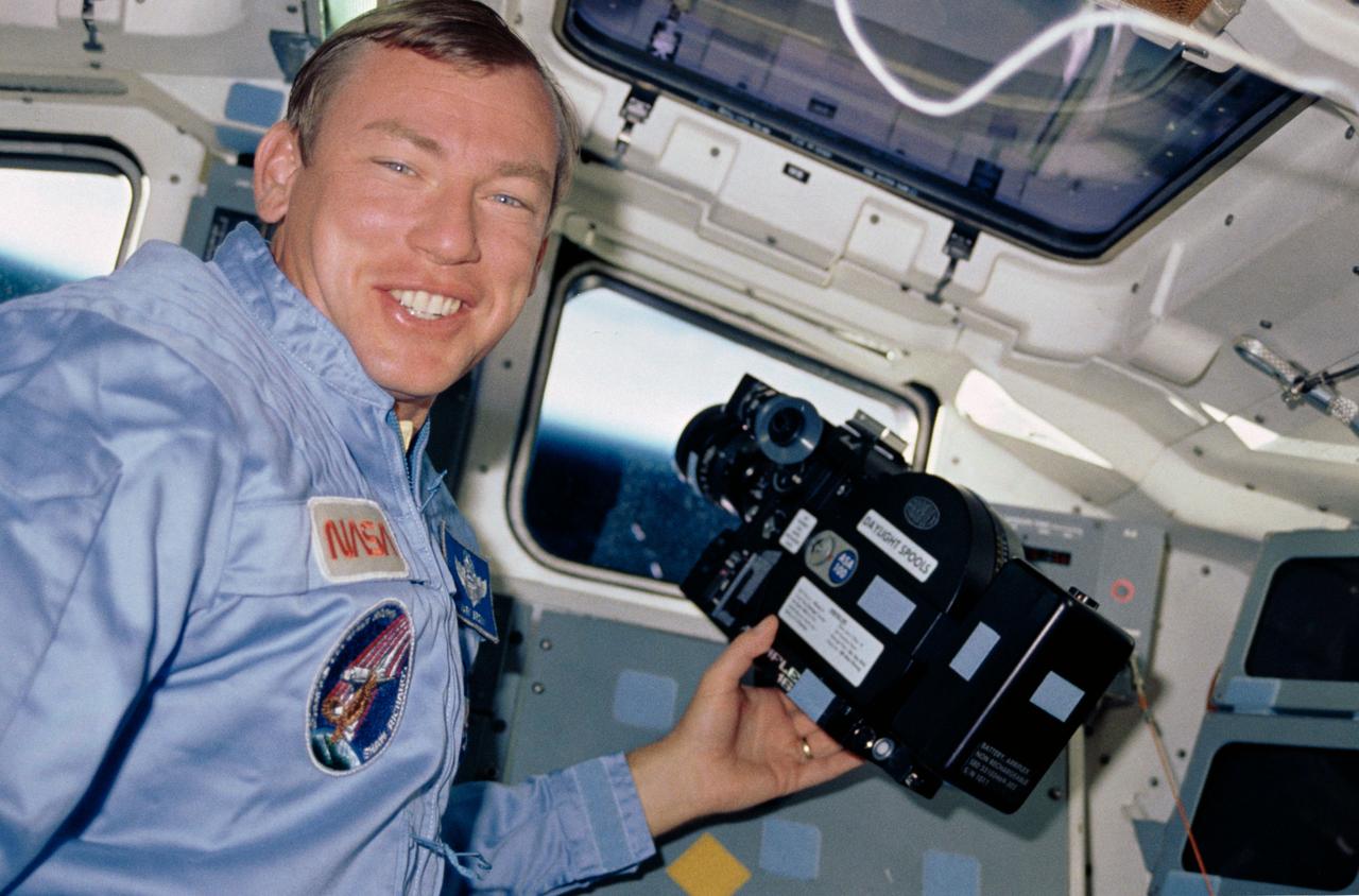 STS028-17-033 (August 1989) --- Astronaut Mark N. Brown, STS-28 mission specialist, pauses from a session of motion-picture photography conducted through one of the aft windows on the flight deck of the Earth-orbiting Space Shuttle Columbia.  He is using an Arriflex camera.  The horizon of the blue and white appearing Earth and its airglow are visible in the background.