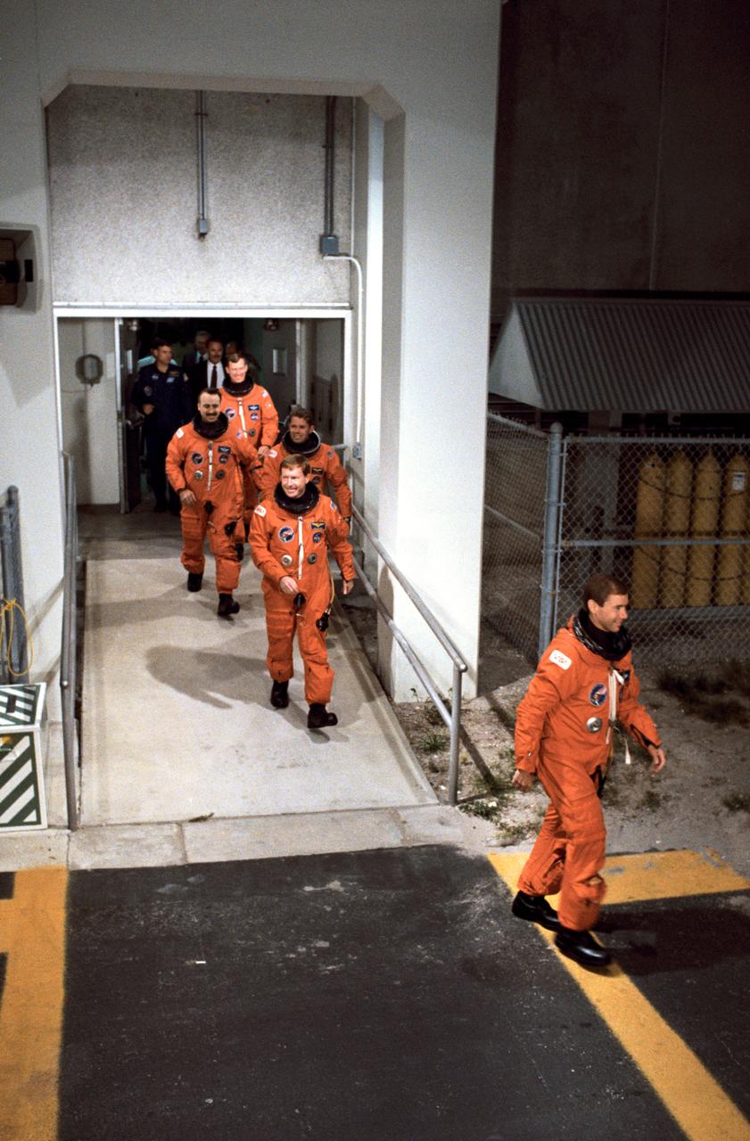 STS028-S-001 (8 Aug 1989) --- The five astronaut crewmembers for STS-28 leave the operations and checkout building to board a transfer van en route to Launch Complex 39 for a date with Columbia. Front to back are Brewster H. Shaw Jr., Richard N. Richards, David C. Leestma, James C. Adamson and Mark N. Brown. At the rear of the line are Astronaut Michael L. Coats, acting chief of the astronaut office; and Donald R. Puddy, director of flight crew operations at JSC. Coats later flew a NASA Shuttle training aircraft for pre-launch and launch monitoring activities.