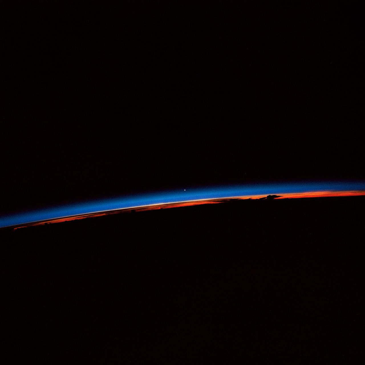 STS-30 Earth observation captured by crewmembers onboard Atlantis, Orbiter Vehicle (OV) 104, shows the sunset over the Earth as well as the planet Venus near the center of the frame. Jutting clouds are seen on the horizon, just beneath the blue strip of airglow.