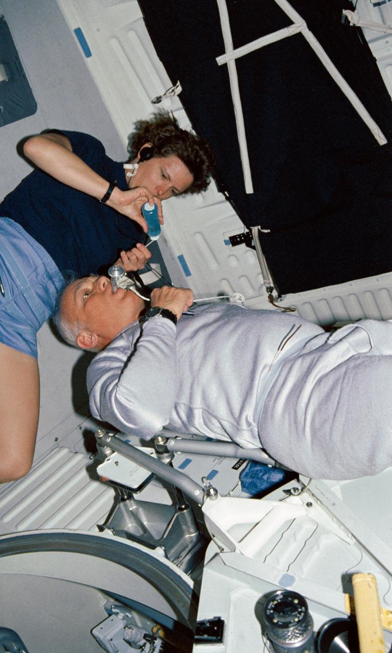 STS031-04-002 (24-29 April 1990) --- Astronauts Kathryn D. Sullivan and Bruce McCandless II, mission specialists, work together to perform one of the mission's medical experiments.  The experiment is Detailed Supplementary Objective (DSO) 462, Non invasive Estimation of Central Venous Pressure During Spaceflight.  Sullivan applies a gel substance to a transducer which will be placed on McCandless' jugular vein to collect the sought data.  The cable links to a data recorder.